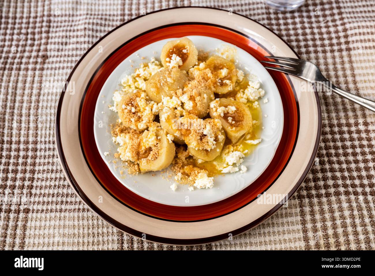 Quark-Aprikosenknödel mit geschmolzener Butter und Brotkrumen auf dekorativem Teller mit Gabel, süßem Essen, Nahaufnahme. Stockfoto