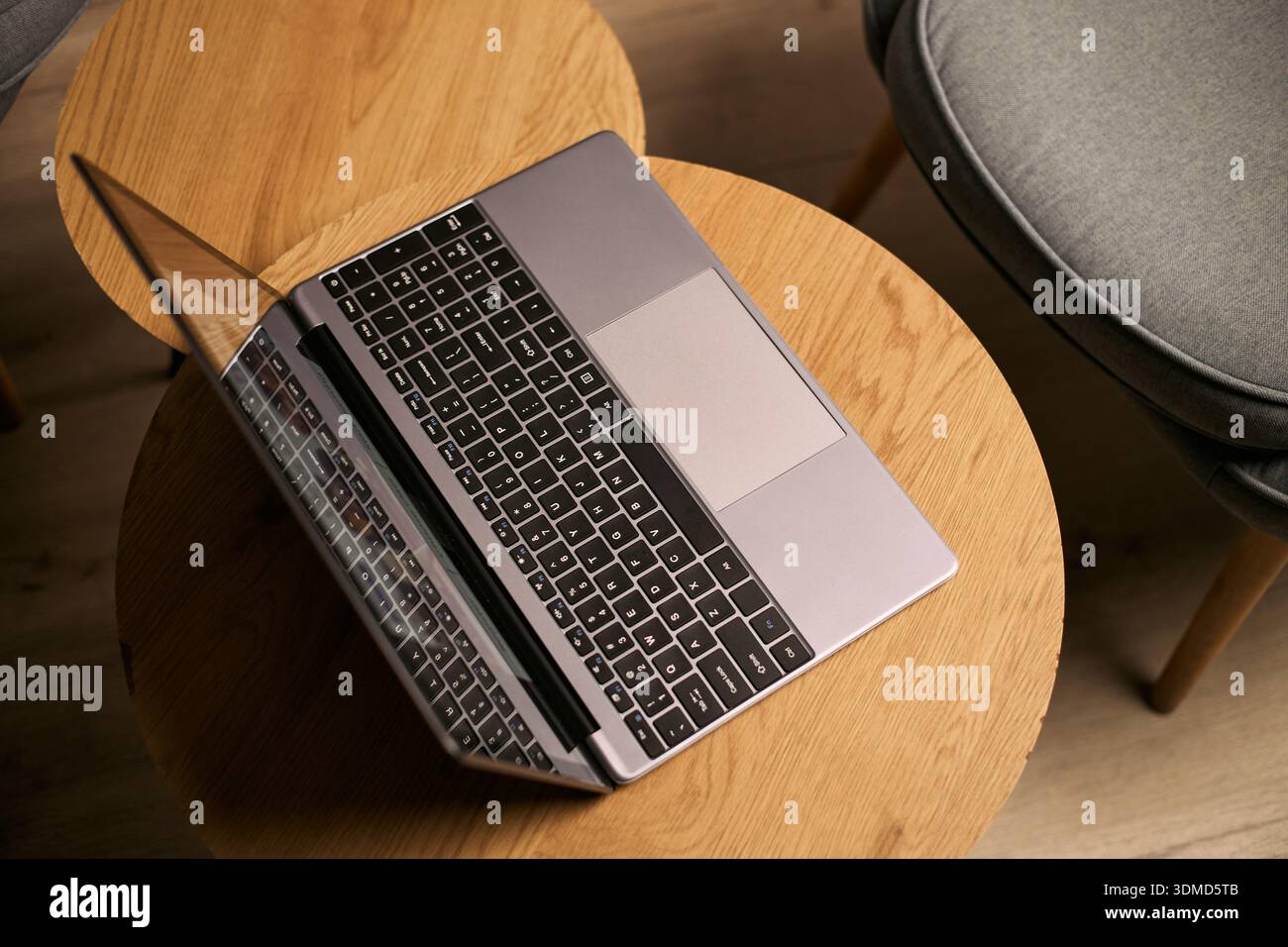 Laptop auf rundem Holztisch im modernen Innenraum, Gerät für Online-Unterricht oder Fernunterricht positioniert, leerer Stuhl neben dem Arbeitsbereich sichtbar Stockfoto