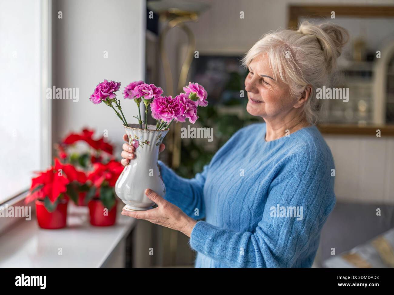 Eine ältere Frau, die zu Hause eine Vase mit Blumen hält Stockfoto