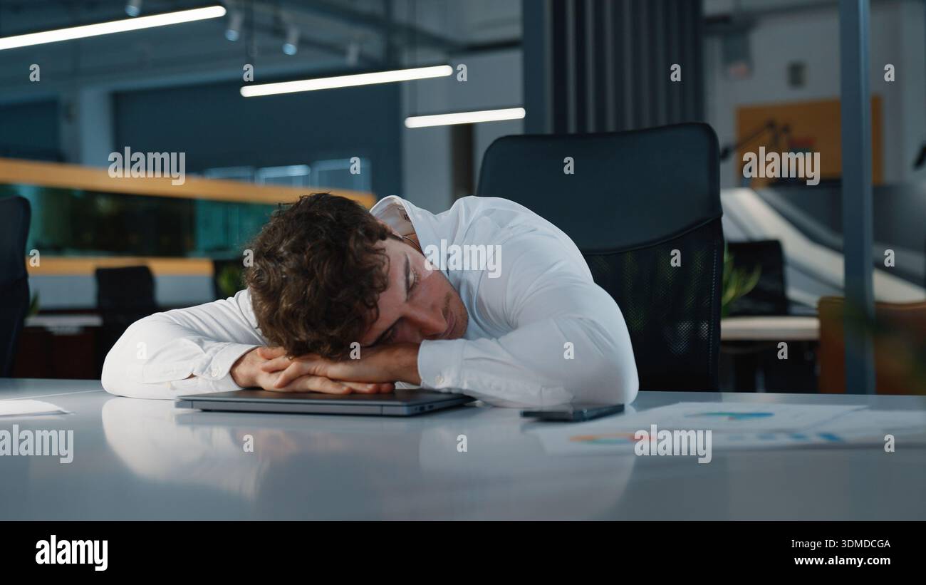 Schläfriger erschöpfter, müder kaukasischer Geschäftsmann beendet die Arbeit, die auf einem geschlossenen Laptop liegt und schläft, auf einem Tisch schläft, Geschäftsmann erledigt die Arbeit, die er schläft Stockfoto