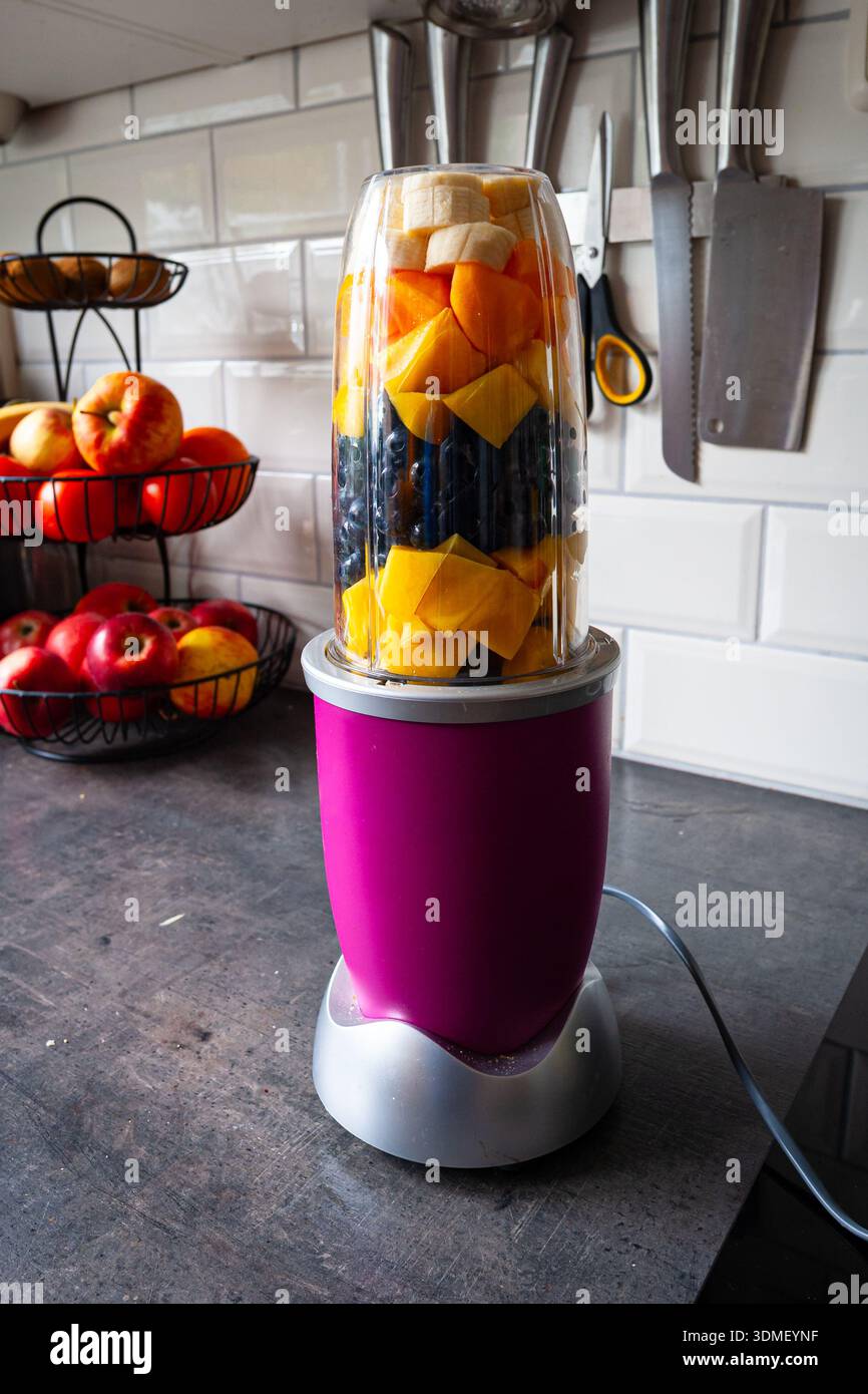 Lebendiger Fruchtmixer auf der Küchenzeile mit frischen Mangos, Heidelbeeren, Pfirsichen und Bananen für gesunden Smoothie Stockfoto