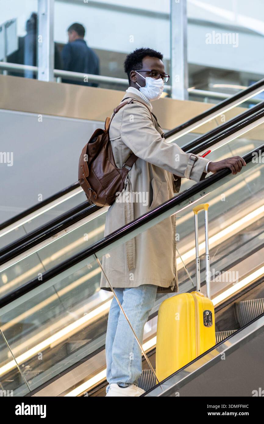 Schwarzer Mann steht auf Rolltreppe im Flughafen tragen Gesichtsmaske, um vor Kontakt mit Nipah-Virus zu schützen Stockfoto