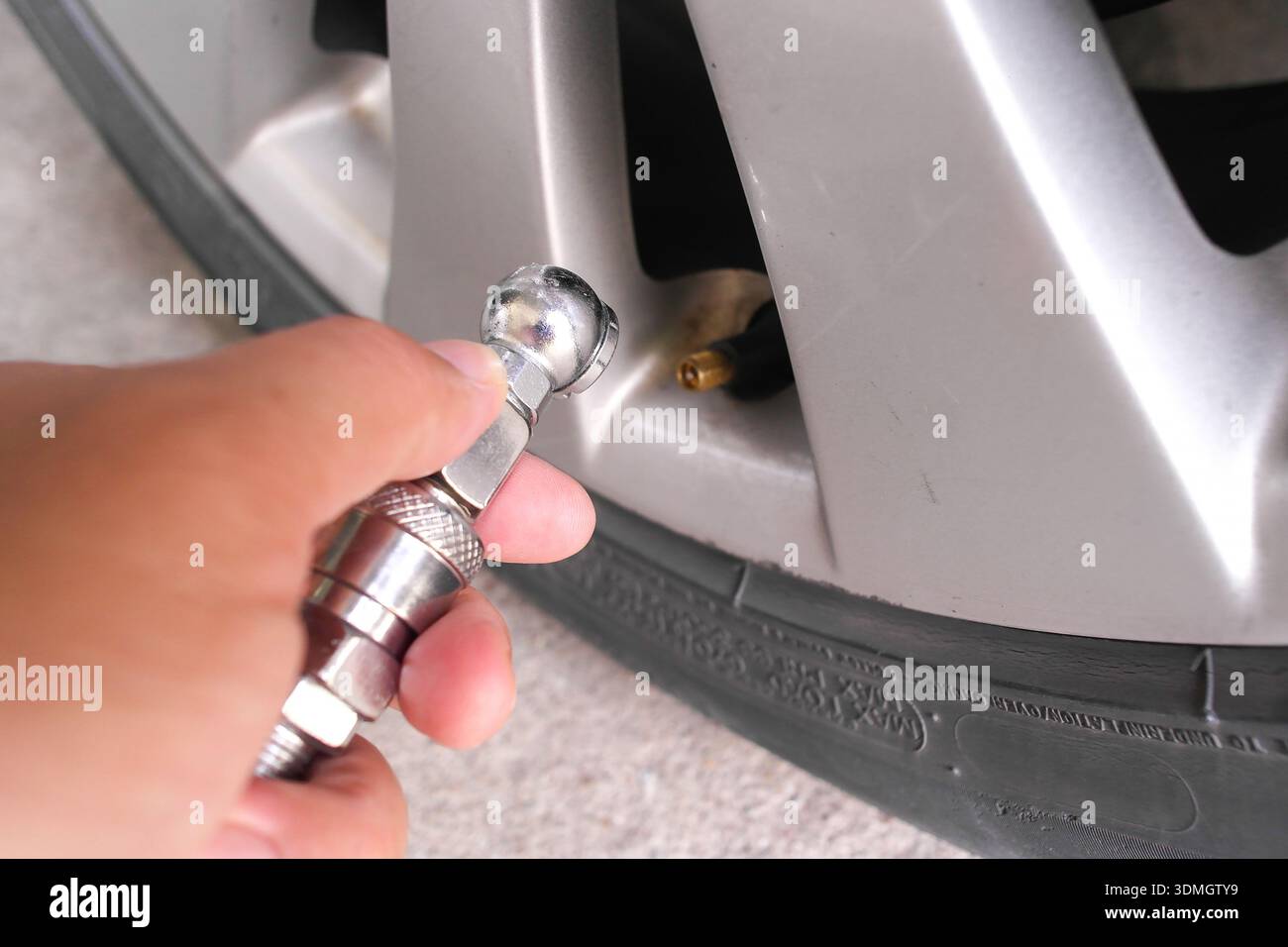Beim Aufpumpen eines Autoreifens bläst die Hand einen Reifen mit einem Metallkugelfuß-Luftspannfutter auf. Stockfoto