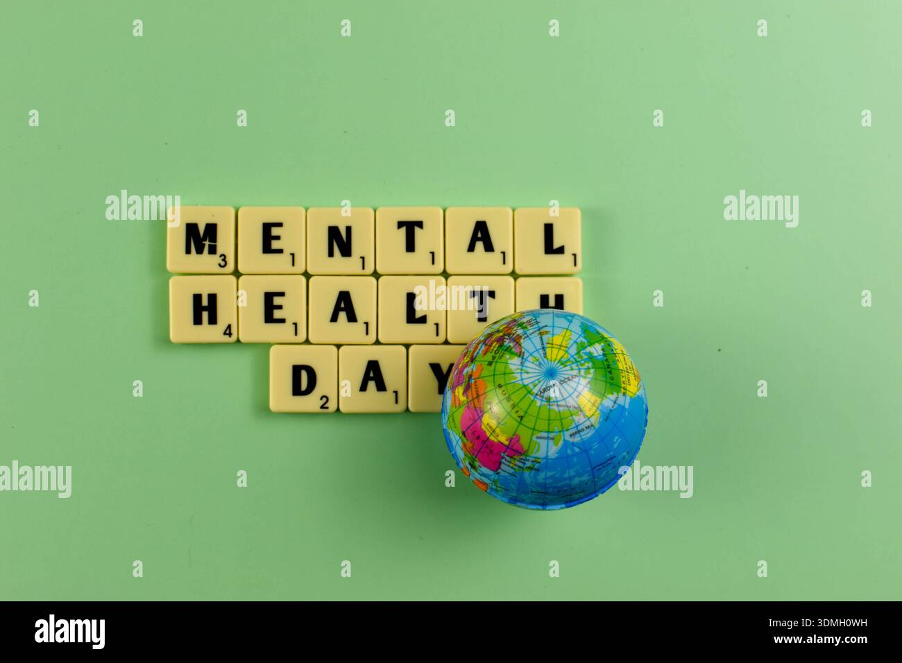 Scrabble-Kacheln schreiben den Tag der mentalen Gesundheit neben dem Globus ein und symbolisieren die globale Anerkennung des emotionalen Wohlbefindens und des Bewusstseins für die mentale Gesundheit. Stockfoto