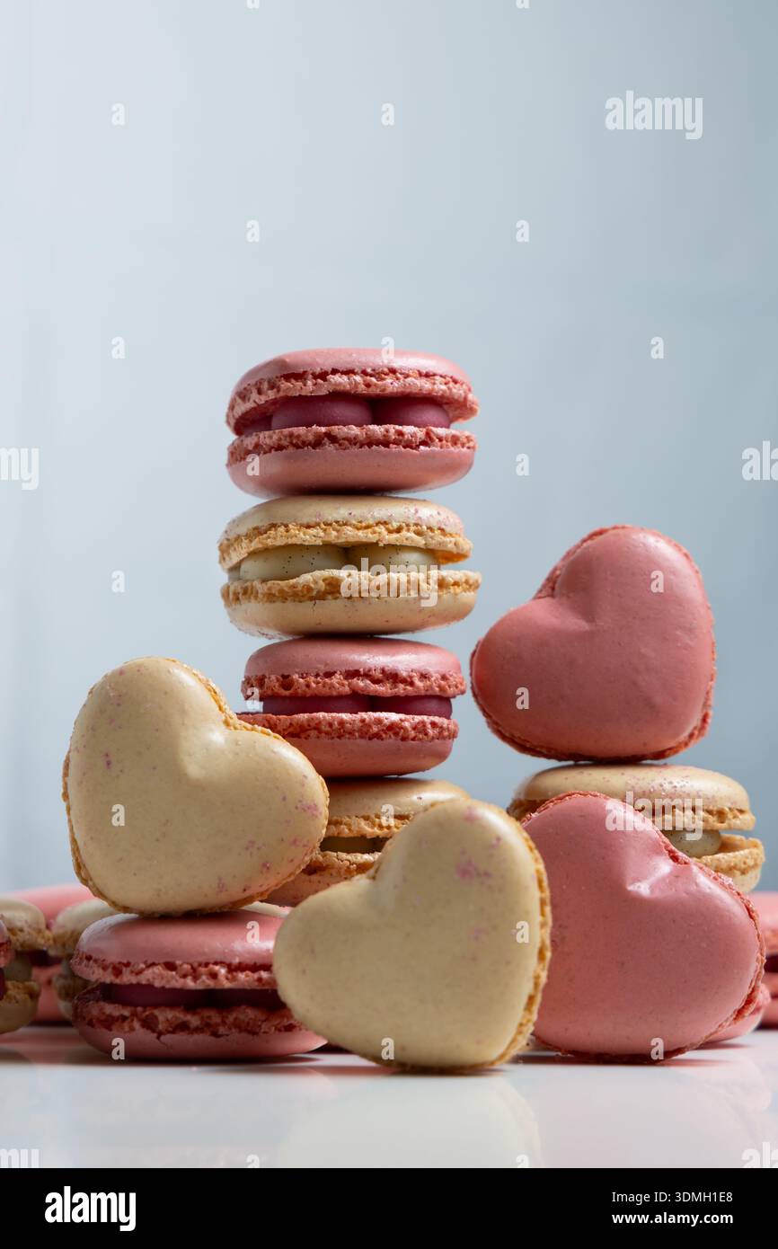 Eine Auswahl von Makaronen wird auf einer weißen Oberfläche platziert. Die Macarons haben sowohl runde als auch herzförmige Formen in Farben wie Rosa und Beige. Stockfoto