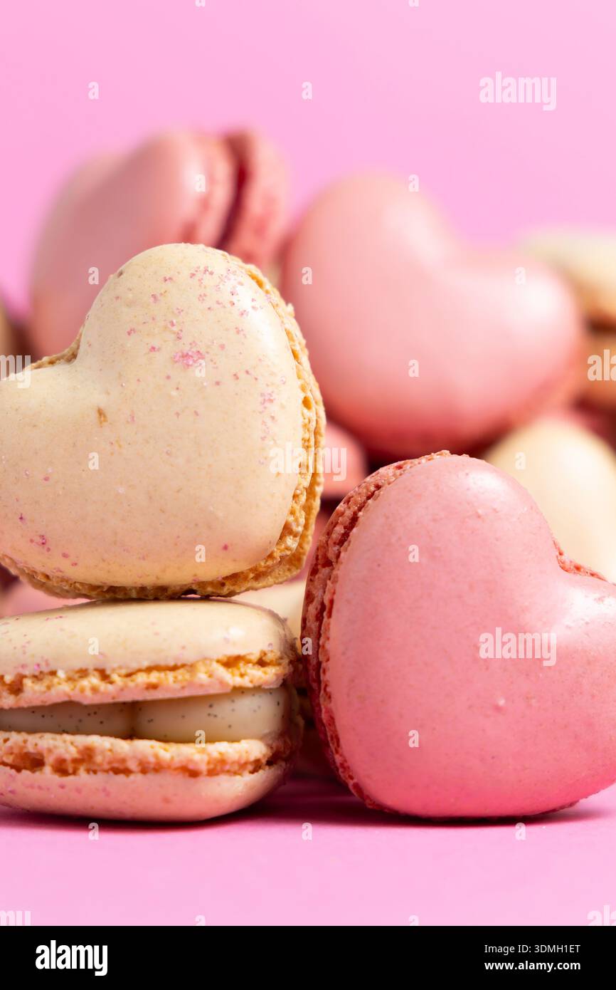Herzförmige Makronen sind in einem Stapel auf rosa Hintergrund angeordnet. Die Macarons sind in zwei Farben erhältlich: Rosa und hellcremefarben. Stockfoto