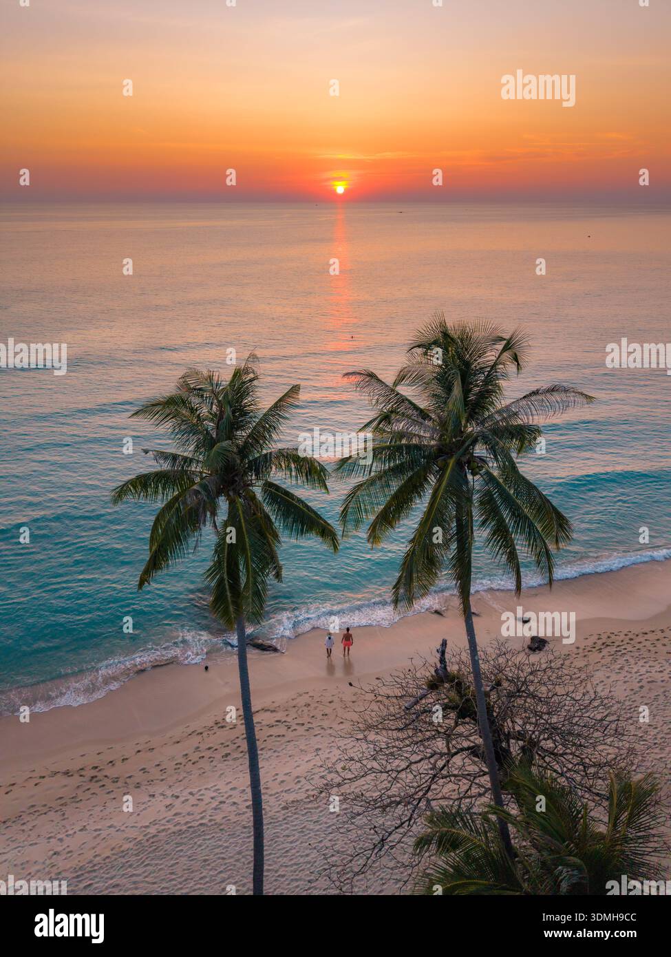Erleben Sie die ruhige Schönheit des Takhian Beach in Koh Kood, Thailand, während die Sonne über ruhigem Wasser untergeht. Ein paar Männer und eine Frau am Strand in der Sonne Stockfoto