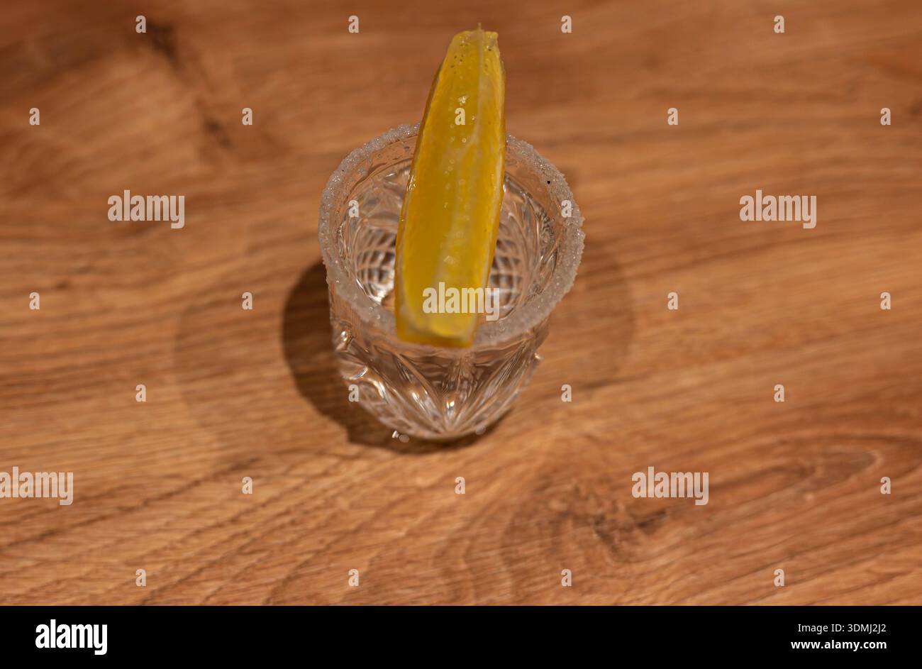 Ein erstklassiger Tequila in einem Kristallglas mit gesalzenem Rand und frischem Zitronenkeil auf einem rustikalen, strukturierten Holztisch. Stockfoto