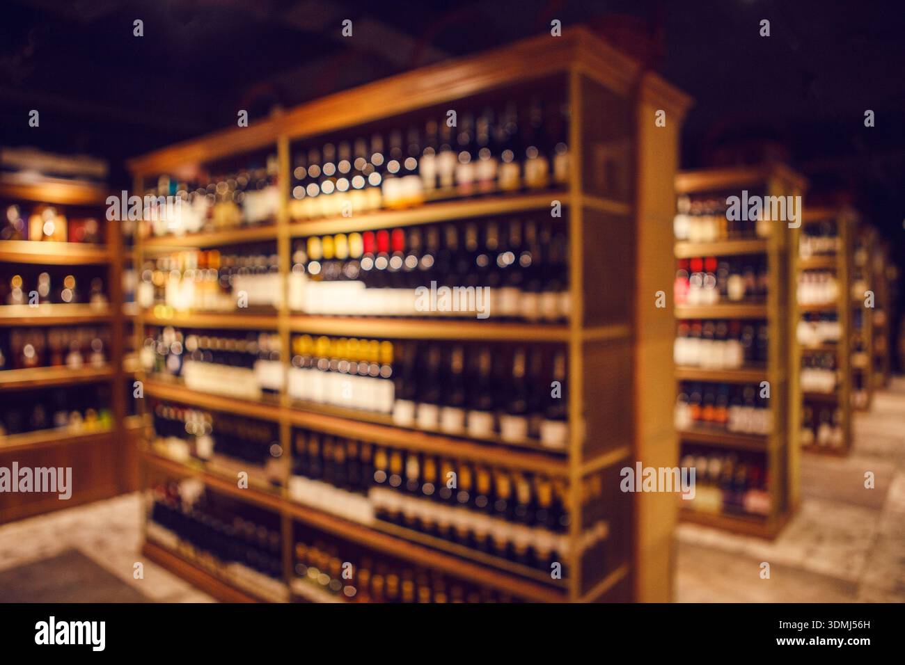 Hohe Weinregale mit gefüllten Flaschen von Elitealkoholgetränken im großen Weinkeller, Unschärfe Foto. Stockfoto