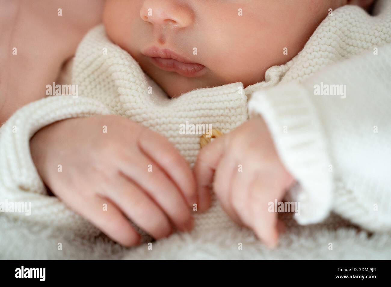 Nahaufnahme eines Neugeborenen mit Fokus auf winzigen Lippen und weichen Händen auf einer Decke. Die geringe Schärfentiefe und der weiche Fokus sorgen für eine sanfte Stockfoto
