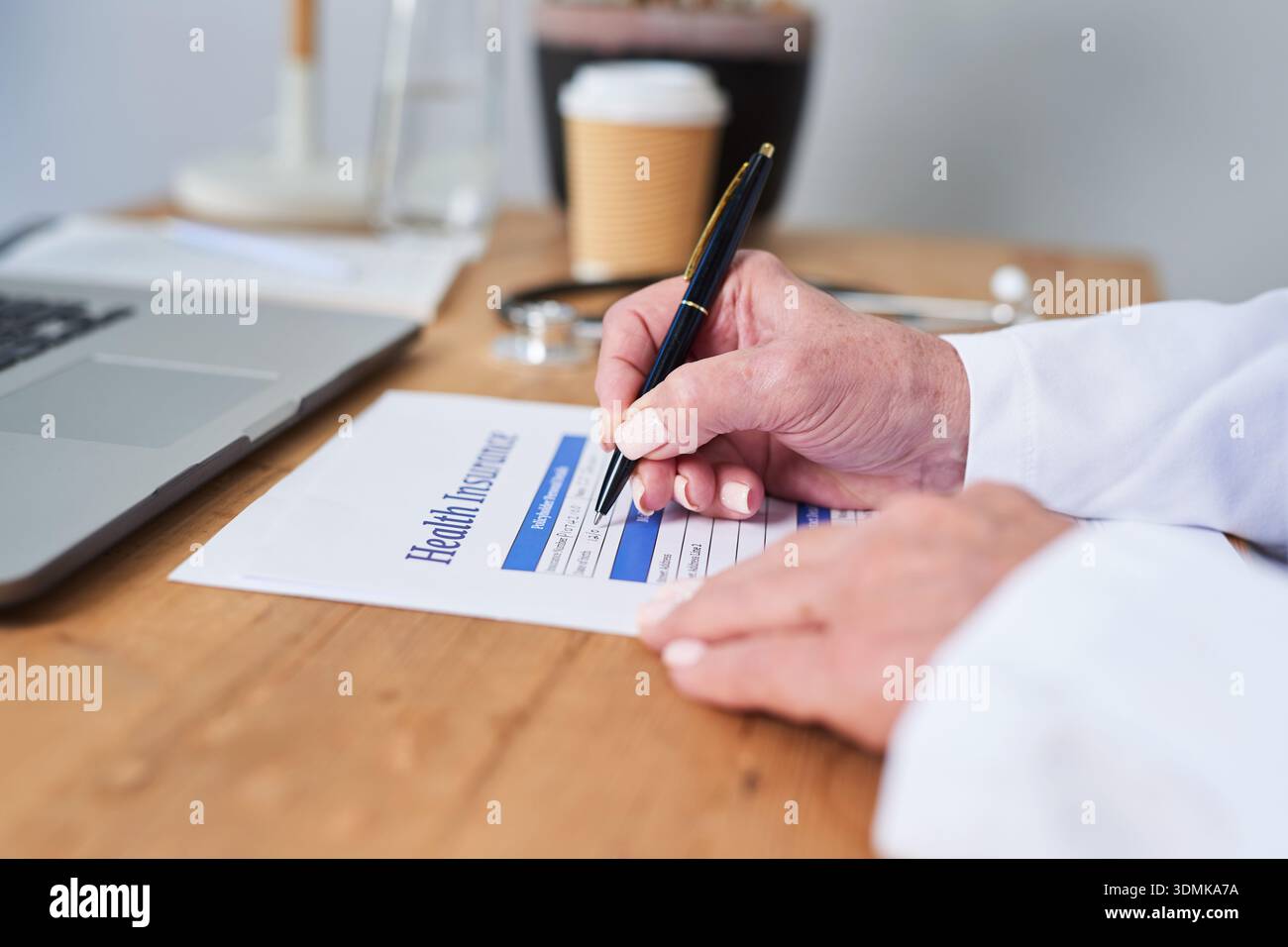 Gesundheitsfachkraft Unterzeichnet Krankenversicherungsformular Am Schreibtisch Mit Laptop Und Kaffee Stockfoto