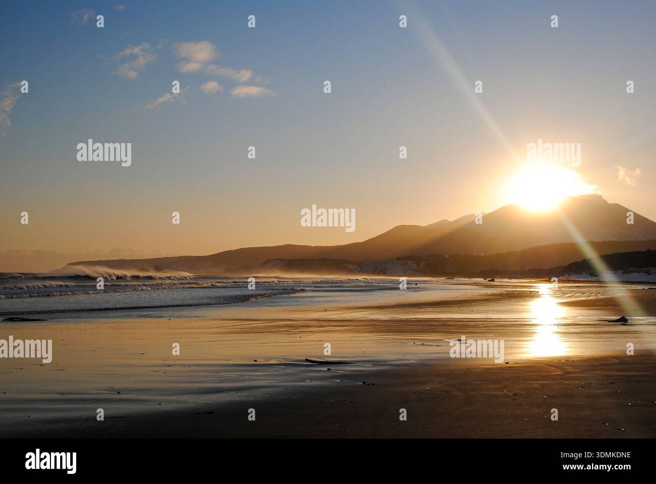 Der Sandstrand einer Bucht der Kurilen Inseln leuchtet wunderschön bei Sonnenuntergang an einem sonnigen Tag. Stockfoto