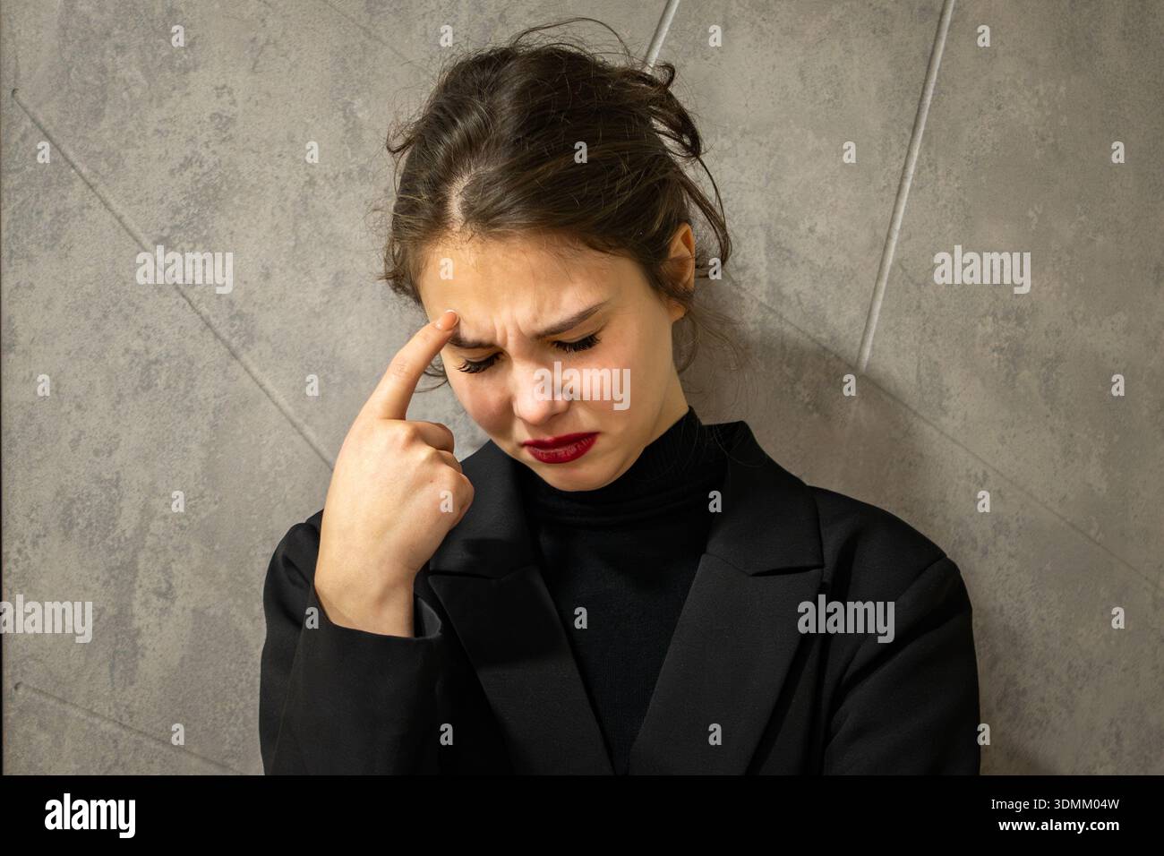 Porträt einer traurigen brünetten Frau, die an einer Wand steht, in Gedanken verloren, besorgt und nachdenklich. Stockfoto
