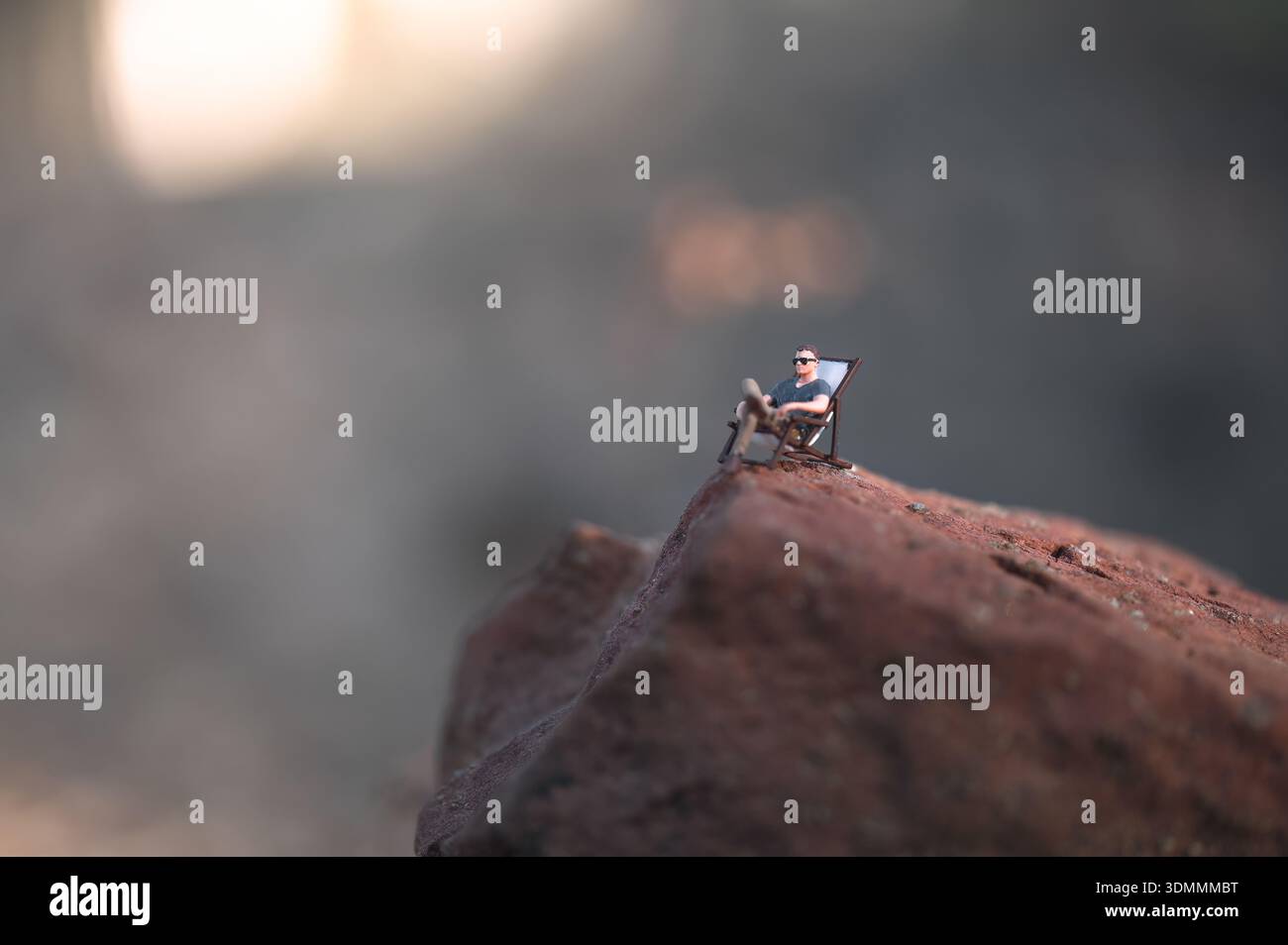 Miniaturfigur, die den Sonnenuntergang von einem Liegestuhl auf einem Felsen aus genießt und Frieden, Ruhe und Ziele symbolisiert Stockfoto