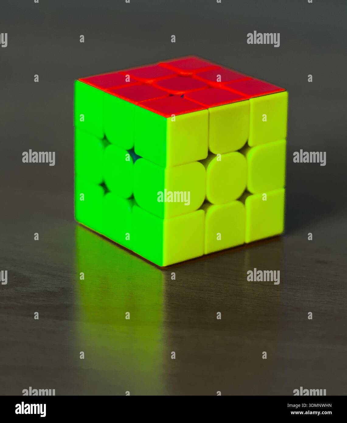 Ein farbenfroher Rubik's Cube mit roten, grünen und gelben Seiten liegt auf einem rustikalen Holztisch, der das ikonische Puzzle in natürlichem Licht zeigt. Stockfoto