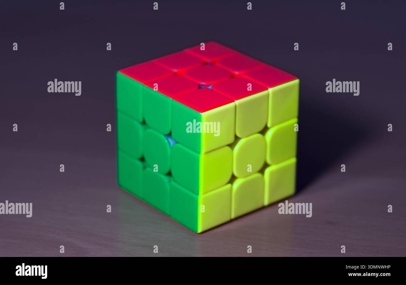 Ein farbenfroher Rubik's Cube mit roten, grünen und gelben Seiten liegt auf einem rustikalen Holztisch, der das ikonische Puzzle in natürlichem Licht zeigt. Stockfoto