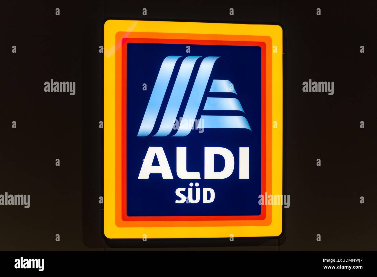 Das beleuchtete ALDI Süd-Logo mit seinen charakteristischen Blau- und Gelbtönen hebt sich vom dunklen Abendhimmel ab und zeigt einen unverkennbaren Einzelhandel Stockfoto