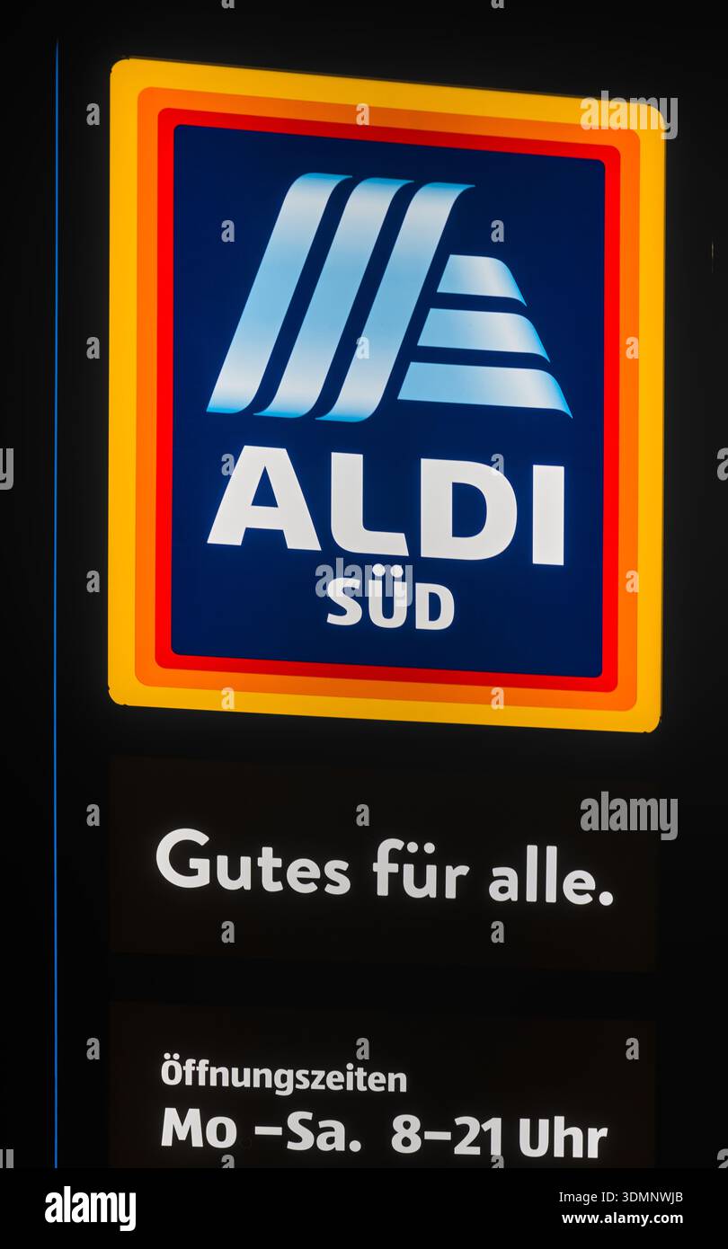 Das beleuchtete ALDI Süd-Logo mit seinen charakteristischen Blau- und Gelbtönen hebt sich vom dunklen Abendhimmel ab und zeigt einen unverkennbaren Einzelhandel Stockfoto