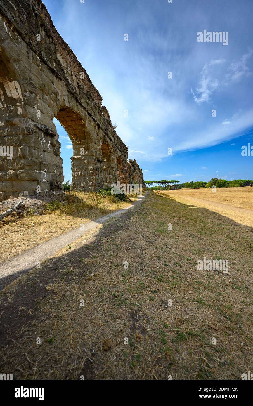 Architektonische Überreste eines römischen Aquädukts inmitten einer offenen Landschaft und Bäumen im Parco degli Acquedotti, Rom. Stockfoto