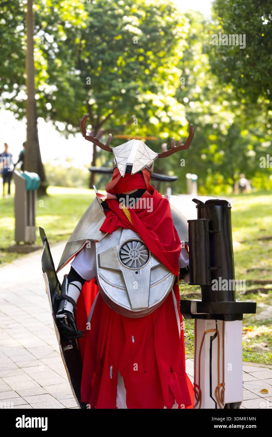 Detailliertes Cosplay einer gepanzerten Figur mit rotem Mantel und gehörntem Helm bei einem Anime-Festival im Freien. Stockfoto