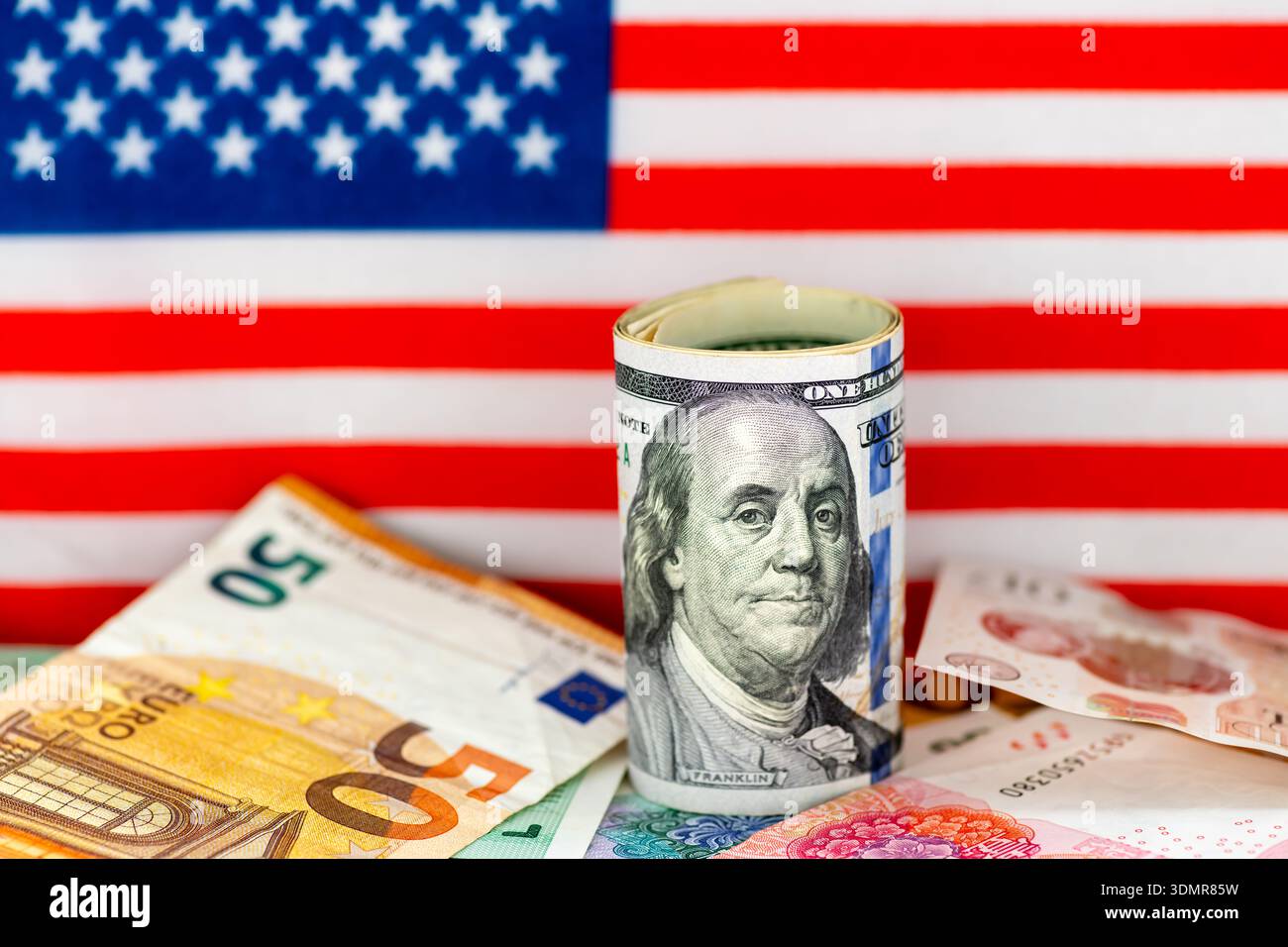 Eine Makroaufnahme einer Rolle von US-Dollar-Scheinen auf anderen Geldscheinen mit der Flagge der Vereinigten Staaten von Amerika im Hintergrund. Stockfoto