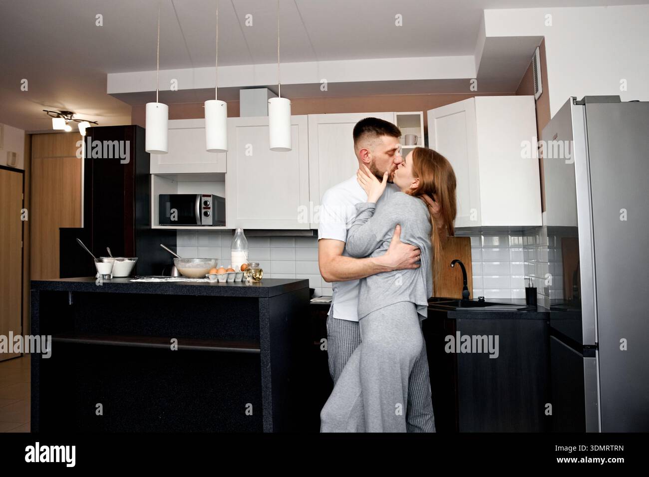 Zwei Leute umarmen sich und küssen sich in einer Küche, während sie sich auf das Frühstück vorbereiten. Sie wirken entspannt und glücklich in ihrer gemütlichen Atmosphäre. Stockfoto