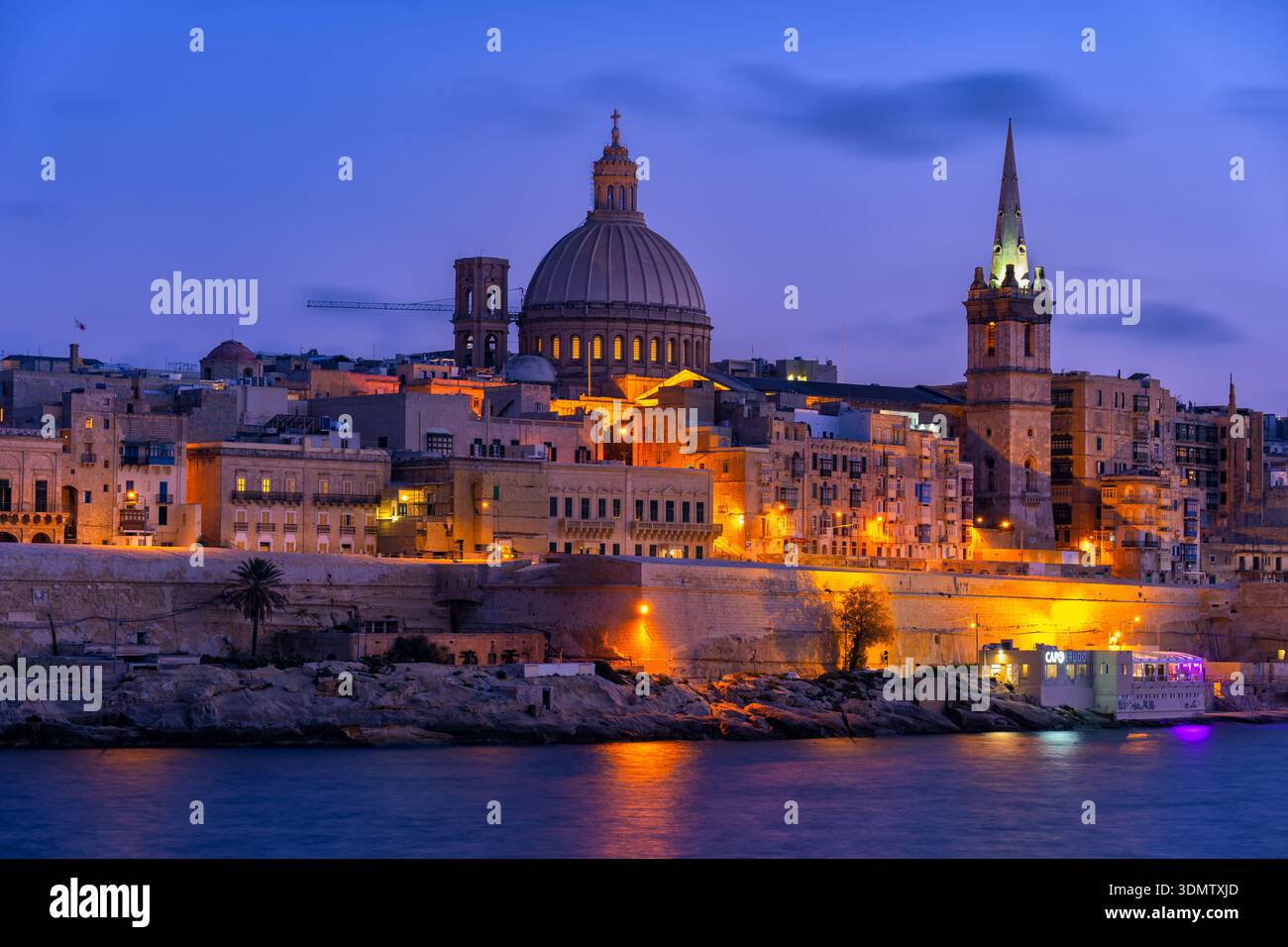 Stadt Valletta (Il-Belt) in der Abenddämmerung auf Malta. Ummauerte Altstadt mit Steinhäusern und Kuppel der Basilika unserer Lieben Frau vom Berg Karmel, Blick vom Marsamx Stockfoto
