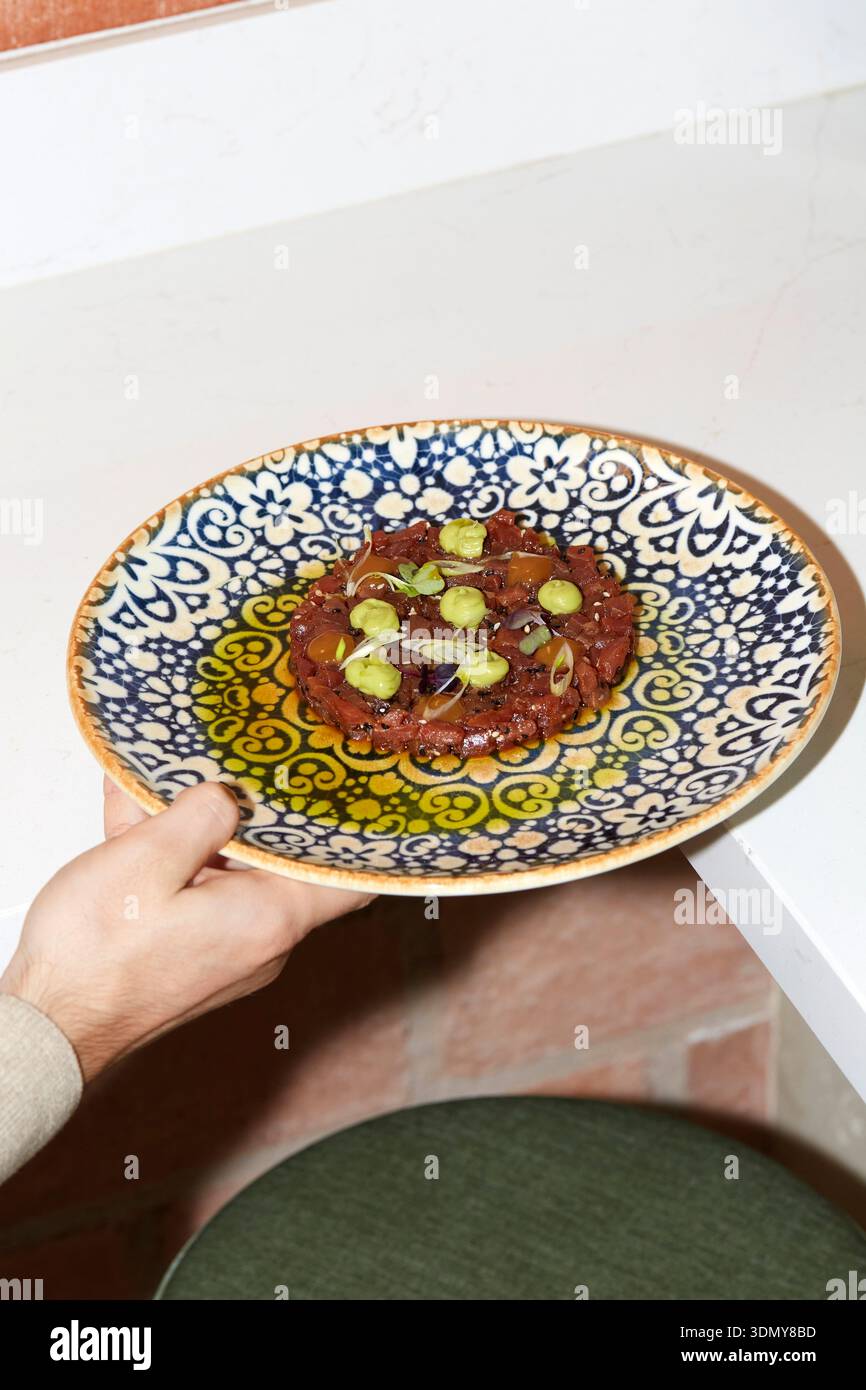 Ein wunderschön überzogenes Gericht, serviert auf einer lebendigen, aufwendig gemusterten Keramikplatte. Die künstlerische Präsentation veranschaulicht die kulinarische Kreativität in A Stockfoto