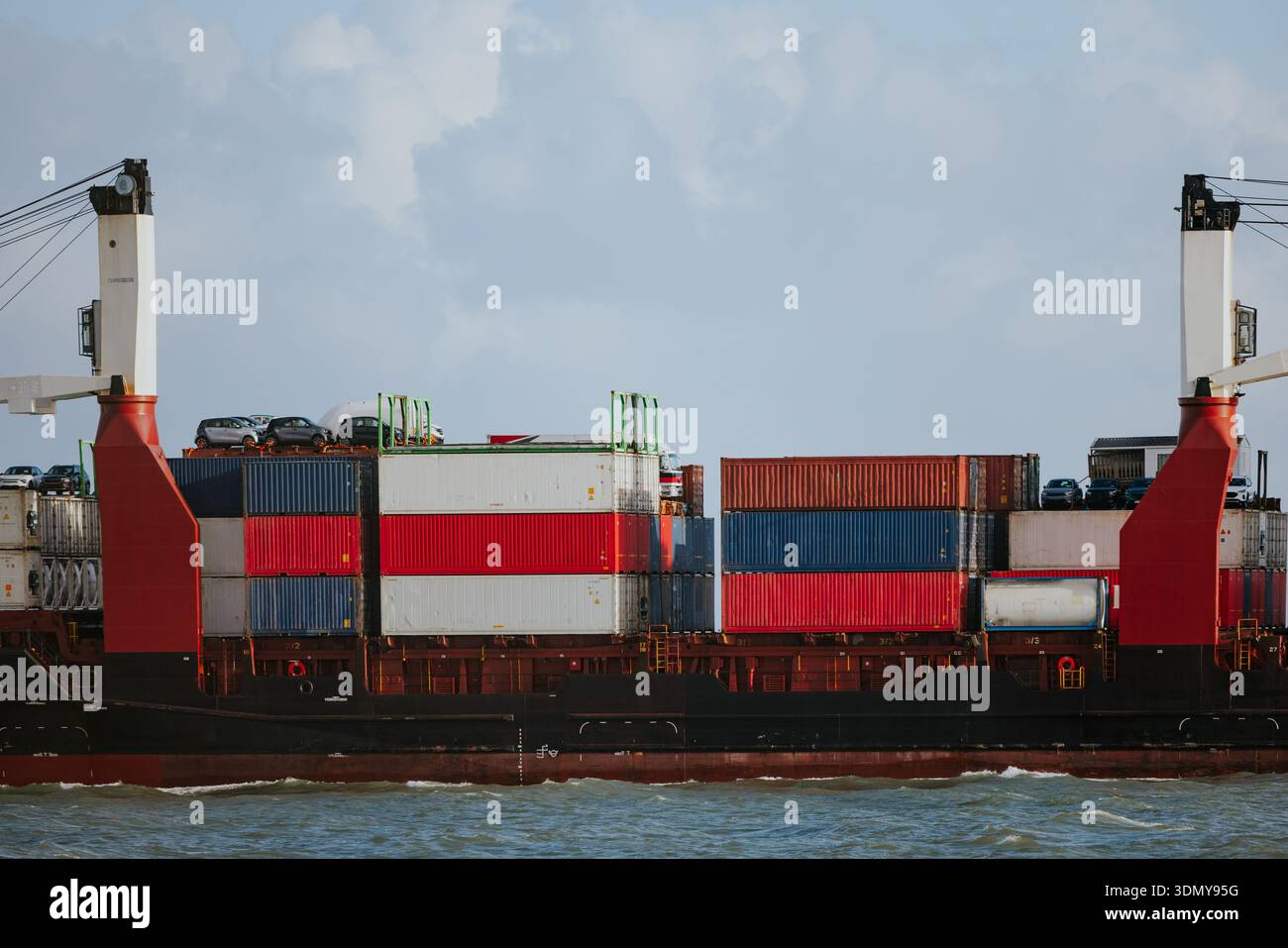 Ein Frachtschiff mit farbenfrohen gestapelten Containern segelt durch ein ruhiges, blaues Meer unter klarem Himmel und zeigt internationalen Handel und Glob Stockfoto