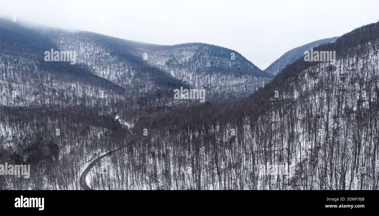 Luftdrohnen-Panorama der verschneiten Catskill Mountains mit einer kurvenreichen Straße durch ein nebeliges Wintertal im Norden von New York. Stockfoto