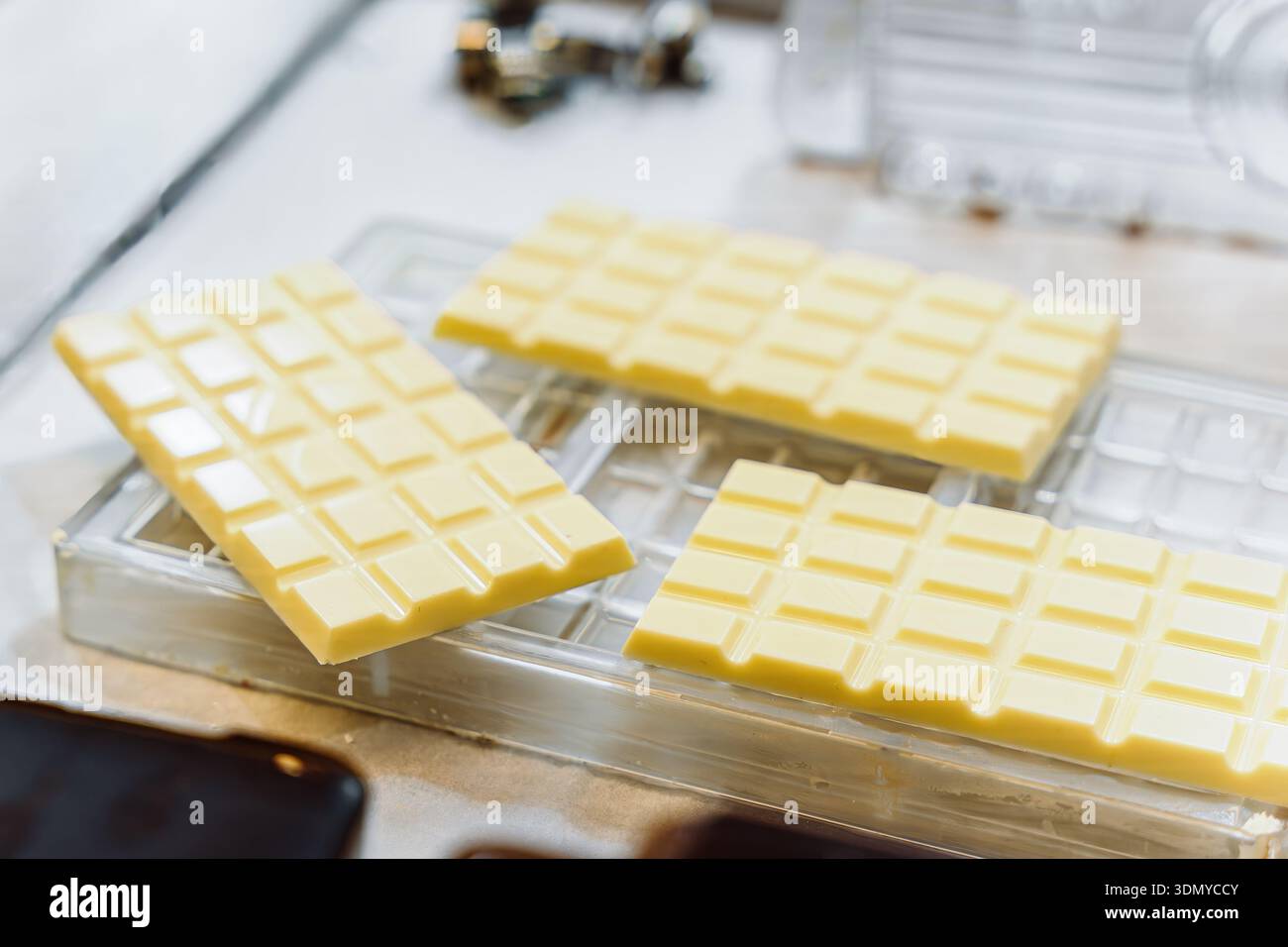 Gehärtete weiße Schokoladentafeln liegen in klaren Formen, die frisch zubereitete weiße Schokoladentafeln verzehrfertig sind Stockfoto
