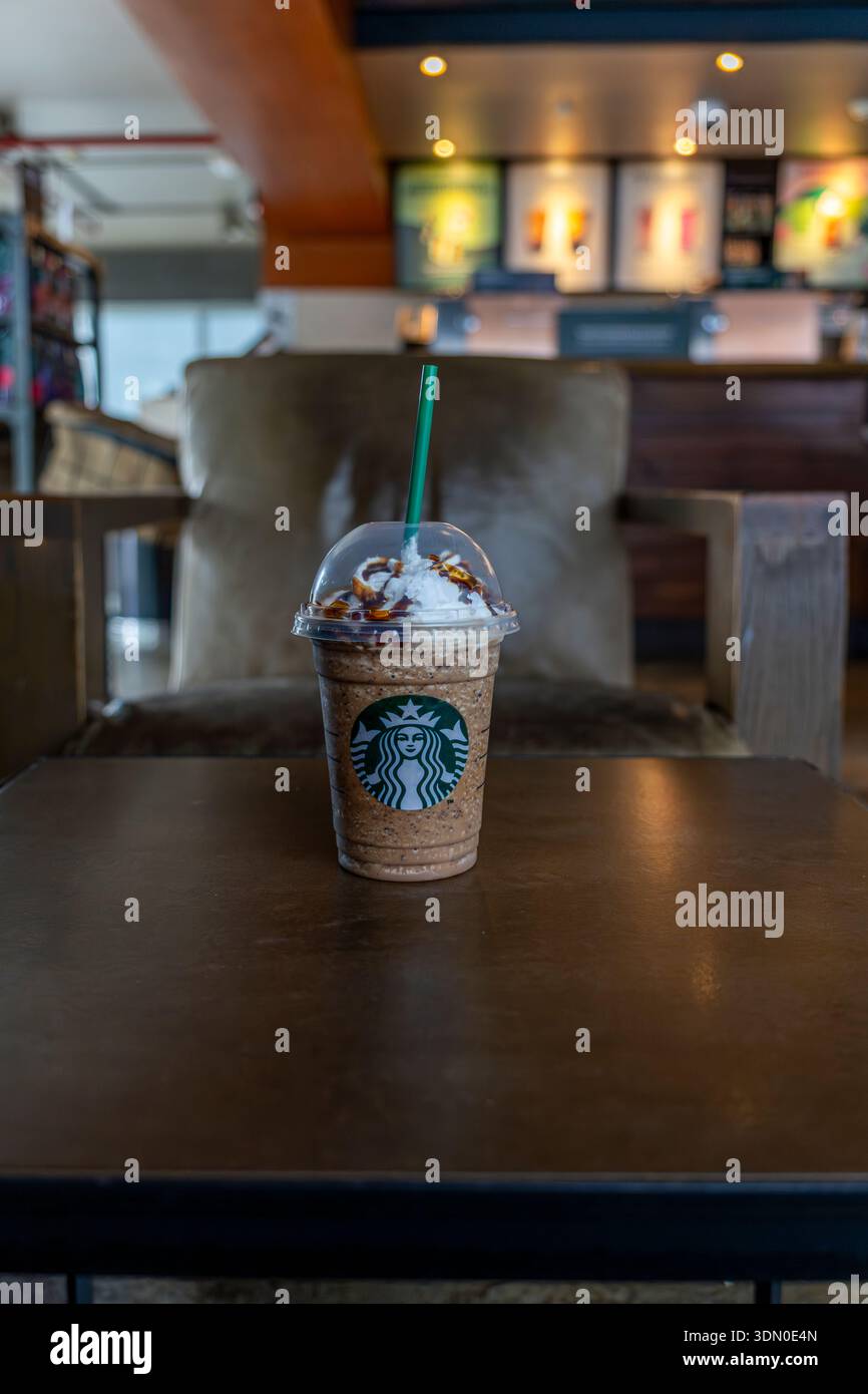 Nur redaktionelle Verwendung. Geeiste Kaffeemischung mit Markenzeichen in einer Plastiktasse zum Mitnehmen mit Schlagsahne und Sirup auf dem Kaffeetisch. Stockfoto
