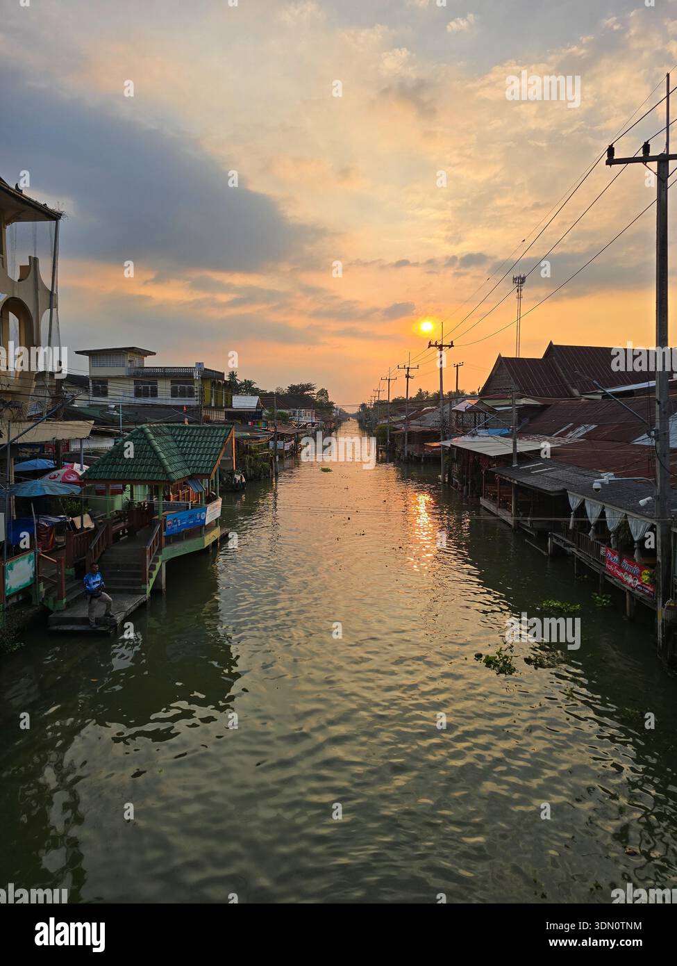 Amphawa Floating Market, Thailand 5. Dezember 2025. Besucher genießen lokale Speisen und Kunsthandwerk entlang des ruhigen Kanals, während die Sonne untergeht und ein warmes Licht ausstrahlt Stockfoto
