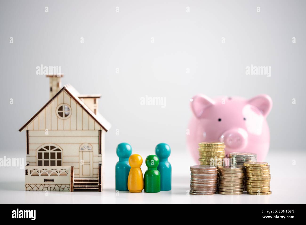 Hypothekensparnis und Familienfinanzplanungskonzept für den Immobilienkauf, mit Miniatur-Holzhaus, farbenfrohen Figuren, Münzstapeln und rosa Stockfoto
