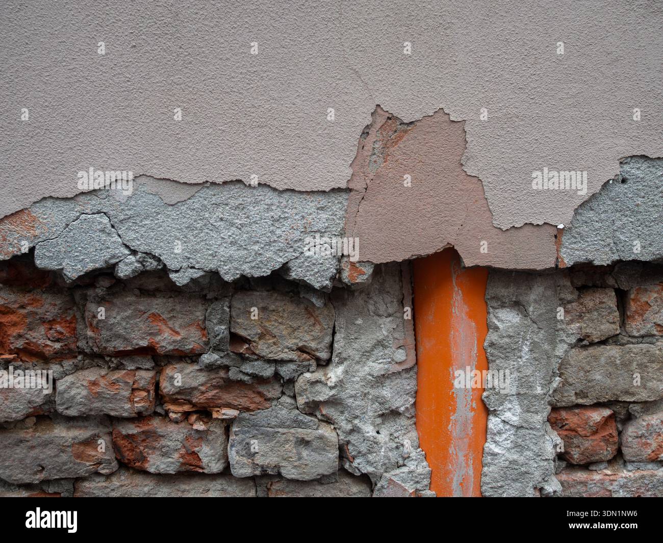 Beschädigte Gebäudefassade mit alten Ziegelmauern und einem orangen Rohr Stockfoto