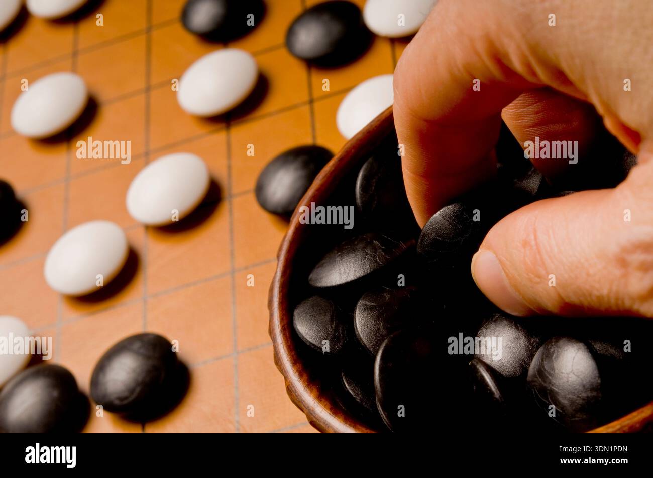 Nahaufnahme einer Hand, die Steine auf ein Go-Board legt, symbolisiert strategisches Denken, Geduld und klassisches abstraktes Brettspiel Stockfoto