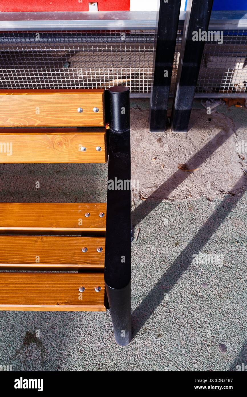 Eine vertikale Hochwinkelaufnahme, die die klaren Linien einer Holzbank, lange Schatten und die farbenfrohen Wandpaneele des Krankenhausgeländes einfängt. Stockfoto