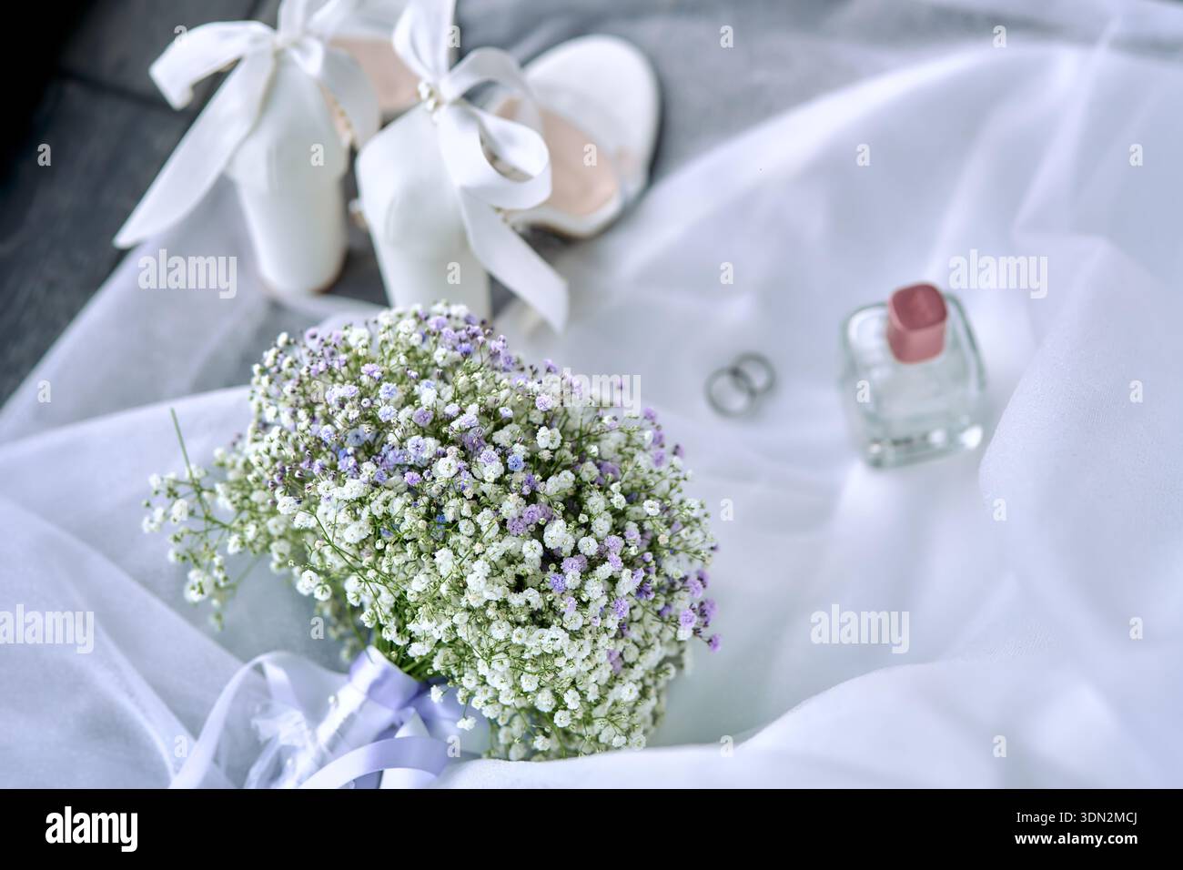 Elegante Hochzeit Flat Lay mit Parfümflasche, Ringen, weißen Schuhen und Blumen auf weißem Stoff Stockfoto