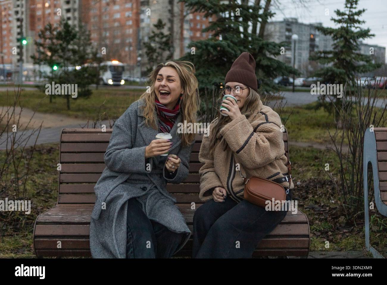 Zwei Frauen in Winterkleidung trinken Kaffee auf der Bank in der bewölkten europäischen Stadt Stockfoto