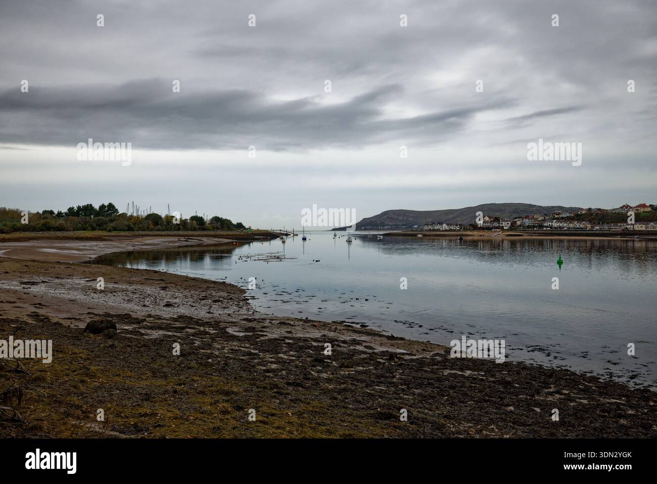 Marmorgrauer Himmel hängt bei Ebbe über den stillen Gewässern einer Mündung mit Yachten, die im mittleren Kanal in Conwy (Conway), Nordwales, ankern. Stockfoto