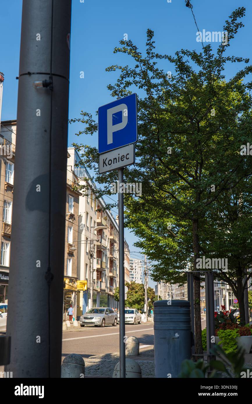 Ein blaues Parkschild mit Koniec markiert das Ende einer Parkzone in Polen. Mittelhohe Wohnhäuser mit Geschäften säumen die Straße, Autos parken an der Bordsteinkante unter freiem Himmel Stockfoto