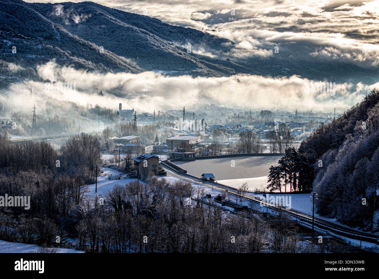 Nebel, der durch ein schneebedecktes Bergtal während des kalten Wintervormittags rollt Stockfoto