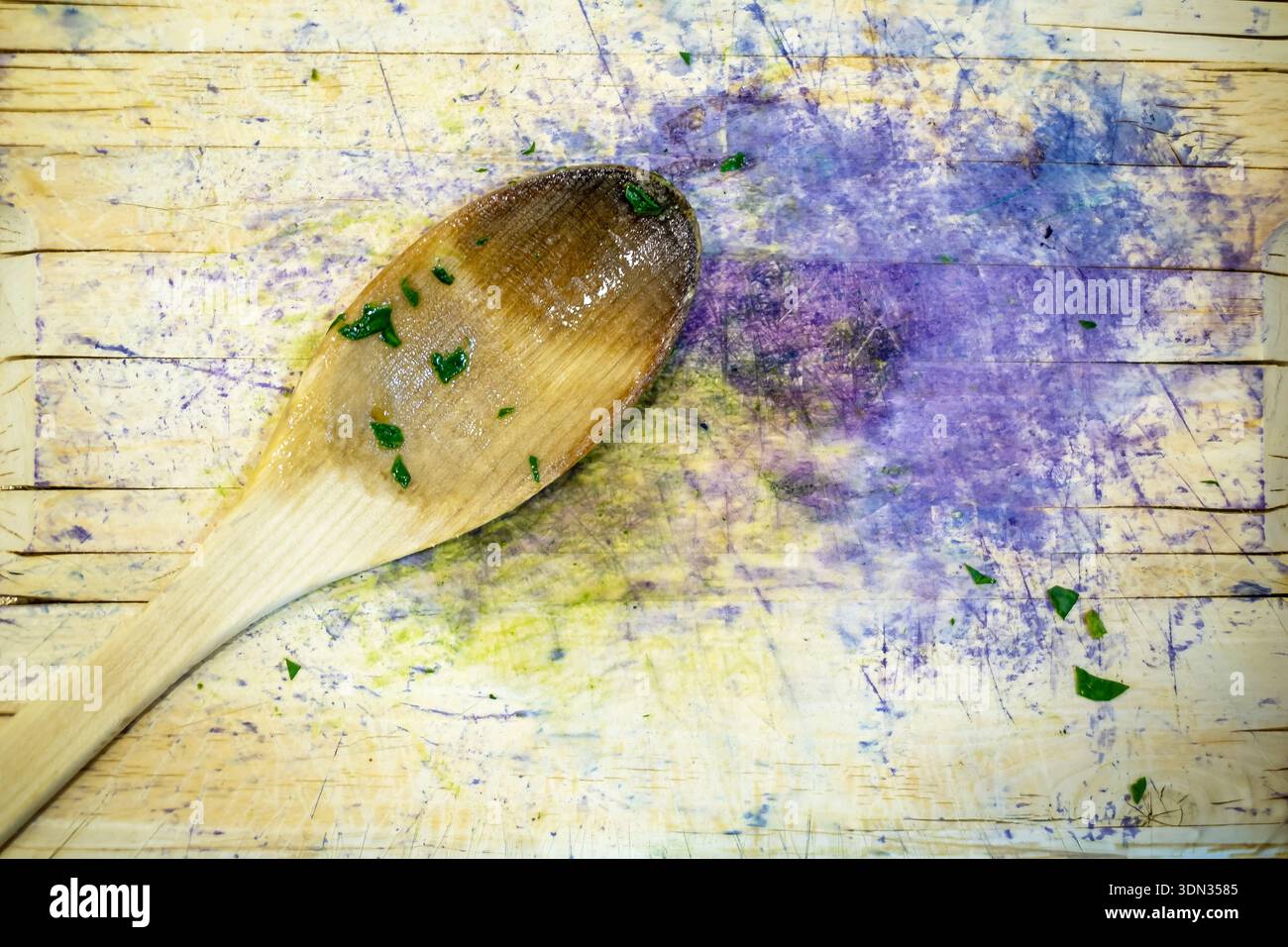 Ein Holzlöffel mit Gemüseresten darauf auf einem Schneidebrett mit Gemüse- und Rotkohlflecken Stockfoto