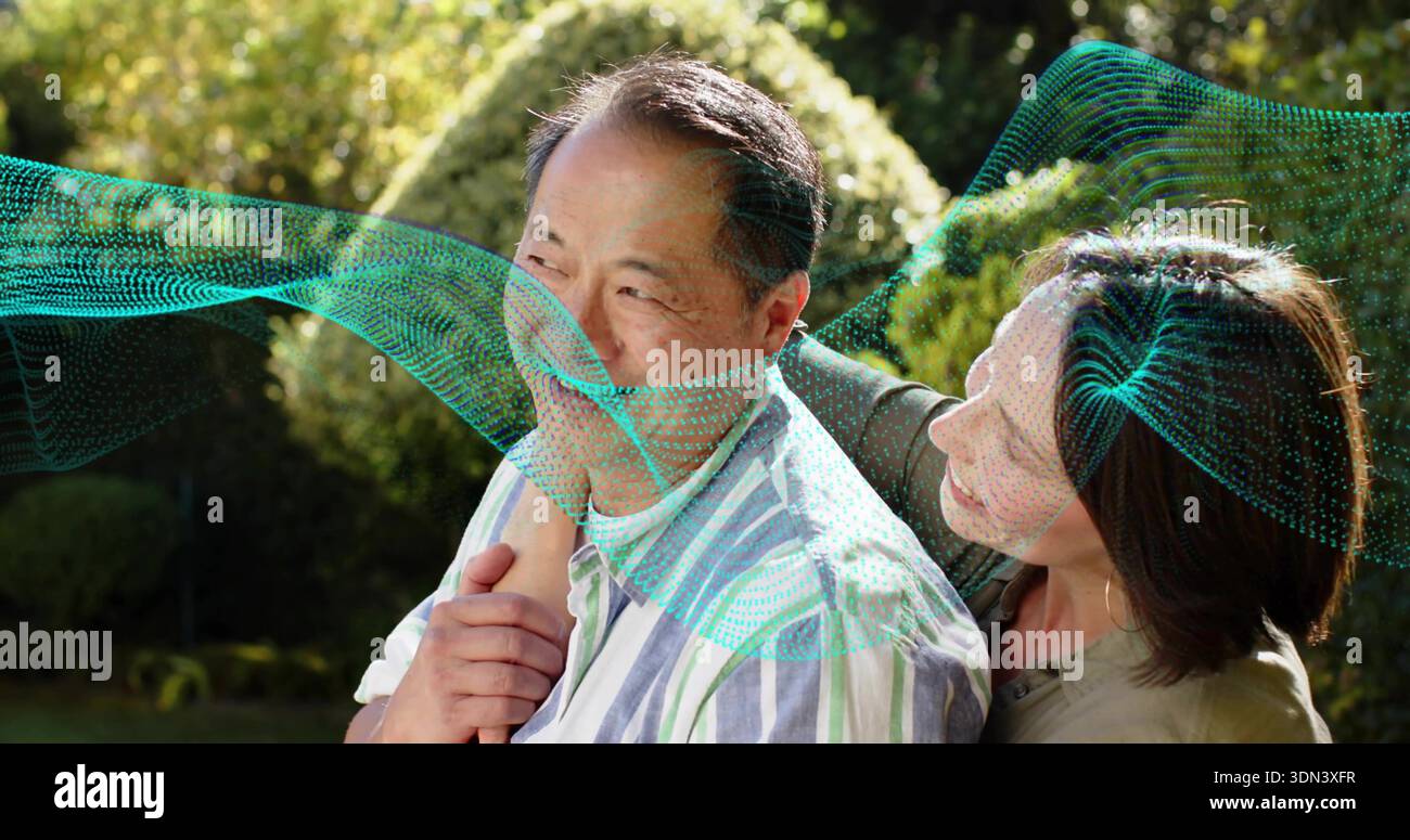 Das ältere Ehepaar, das im Garten steht, trägt ein gestreiftes Hemd und ein olivfarbenes Oberteil, das türkisfarbene Wellen zeigt Stockfoto