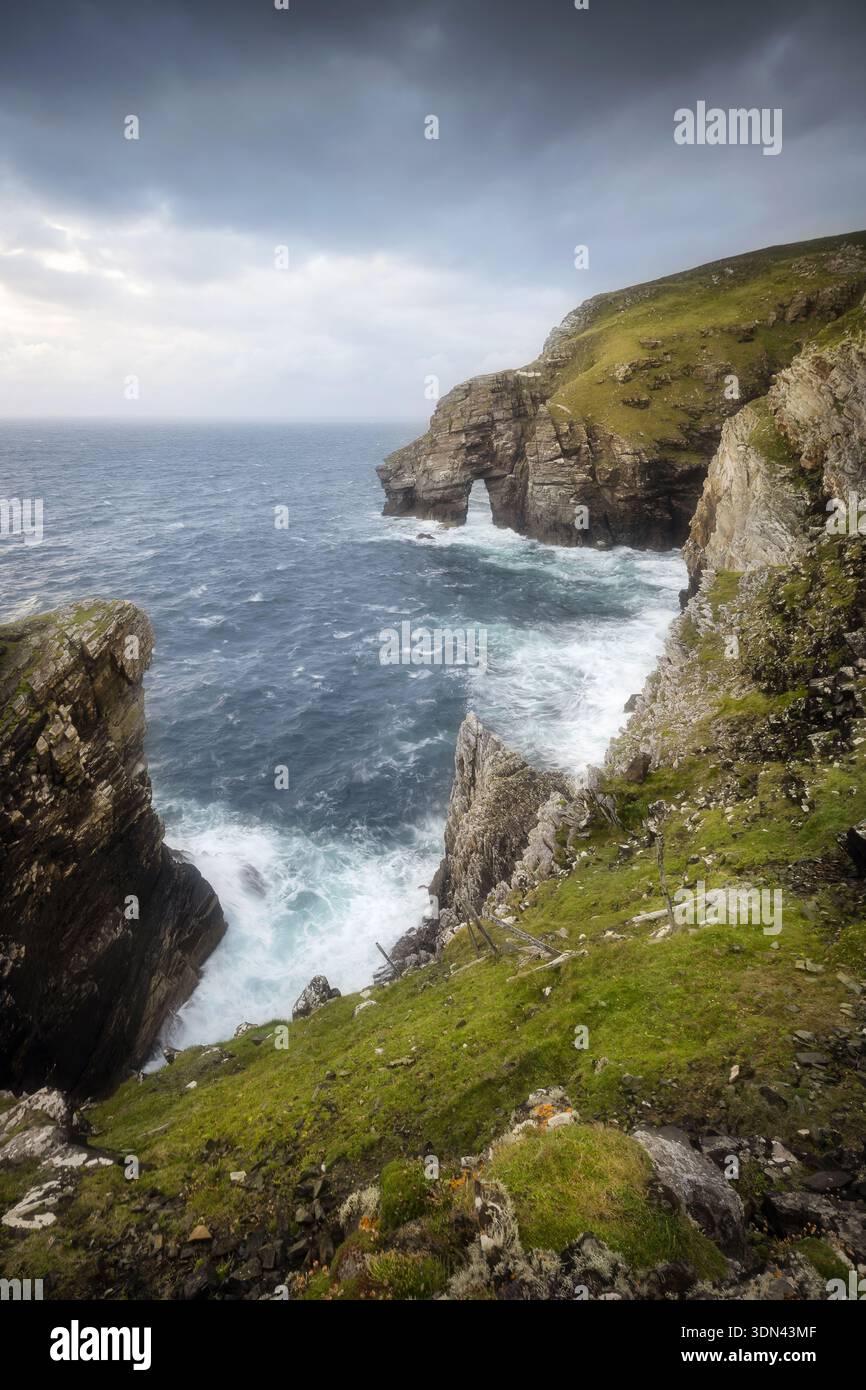 Der Blick auf dramatische Klippen trifft auf das turbulente Meer unter einem stürmischen Himmel, während Wellen gegen die zerklüftete Küste von Dunfanaghy, County Donegal, Irland, krachen. Stockfoto