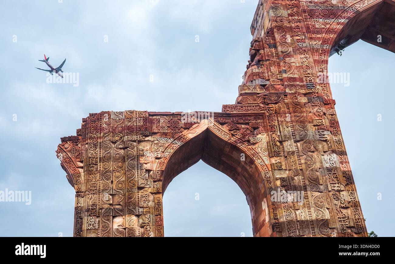 Modernes kommerzielles Flugzeug, das über die antiken Ruinen des Qutub Minar Complex in Delhi, Indien, mit komplizierten Sandsteinschnitzereien und historischem islamischen Bogen fliegt Stockfoto