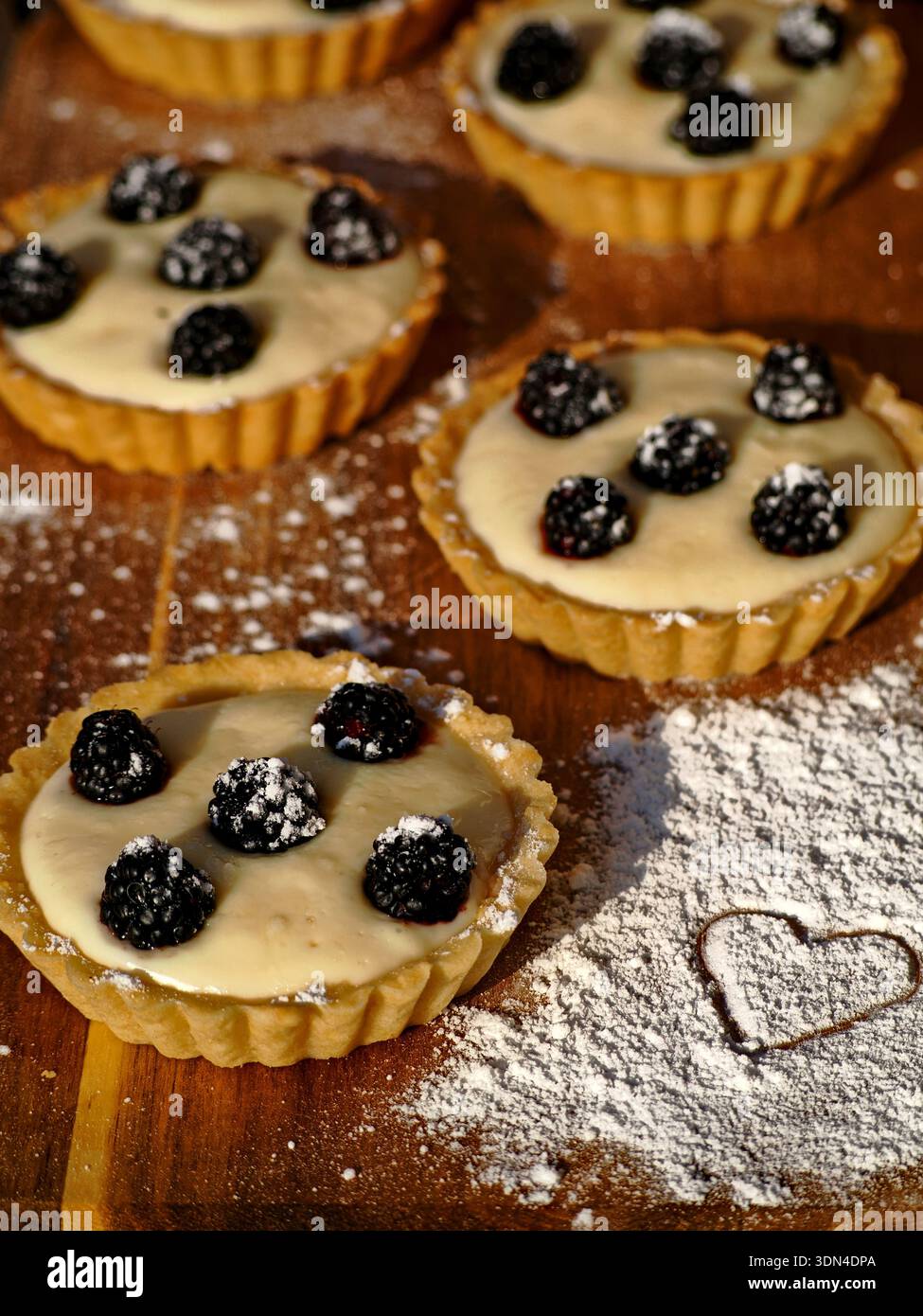 Tartlets mit Beerenfüllung, Puderzucker auf Holzbrett und Herzmehl-Prägung. Stockfoto