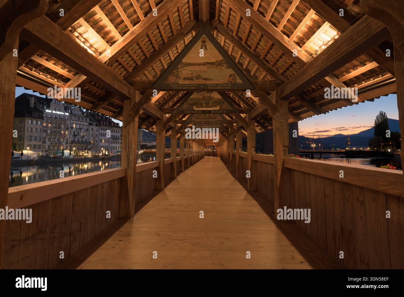 Die Kapellbrücke in Luzern, Schweiz, strahlt mit warmen Innenleuchten und reflektiert die Reuss, während die Dämmerung sich über der Stadt niederschlägt Stockfoto