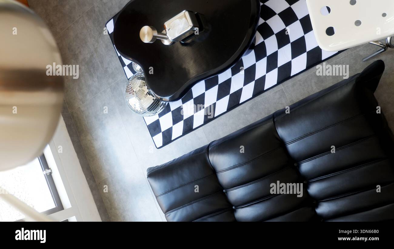 Blick von oben auf modernes Interieur mit schwarzem Ledersofa und kariertem Teppich Stockfoto