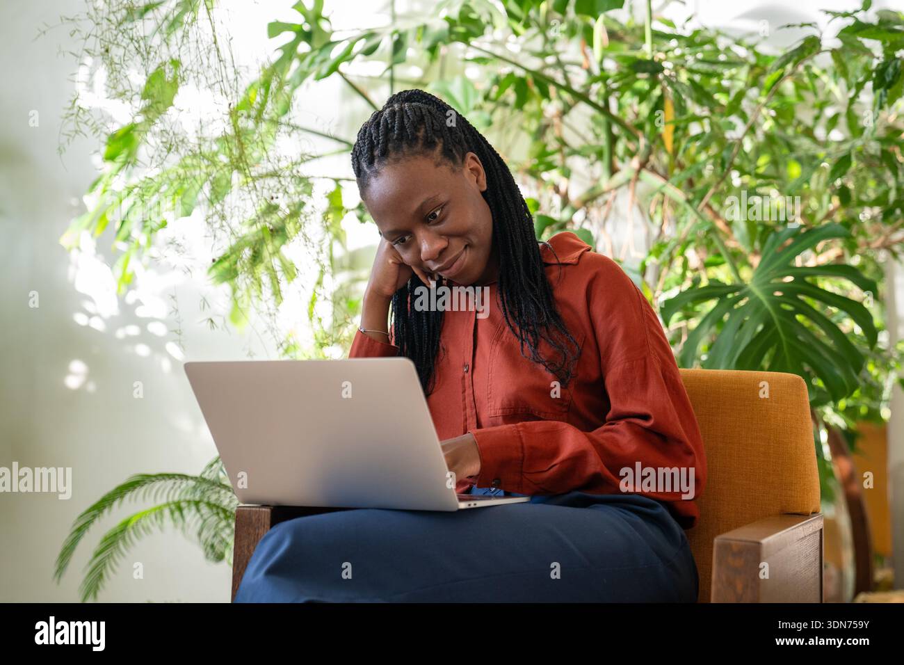 Entspannt lächelnde afroamerikanische Geschäftsfrau arbeitet mit Laptop in einem gemütlichen grünen tropischen Garten. Stockfoto